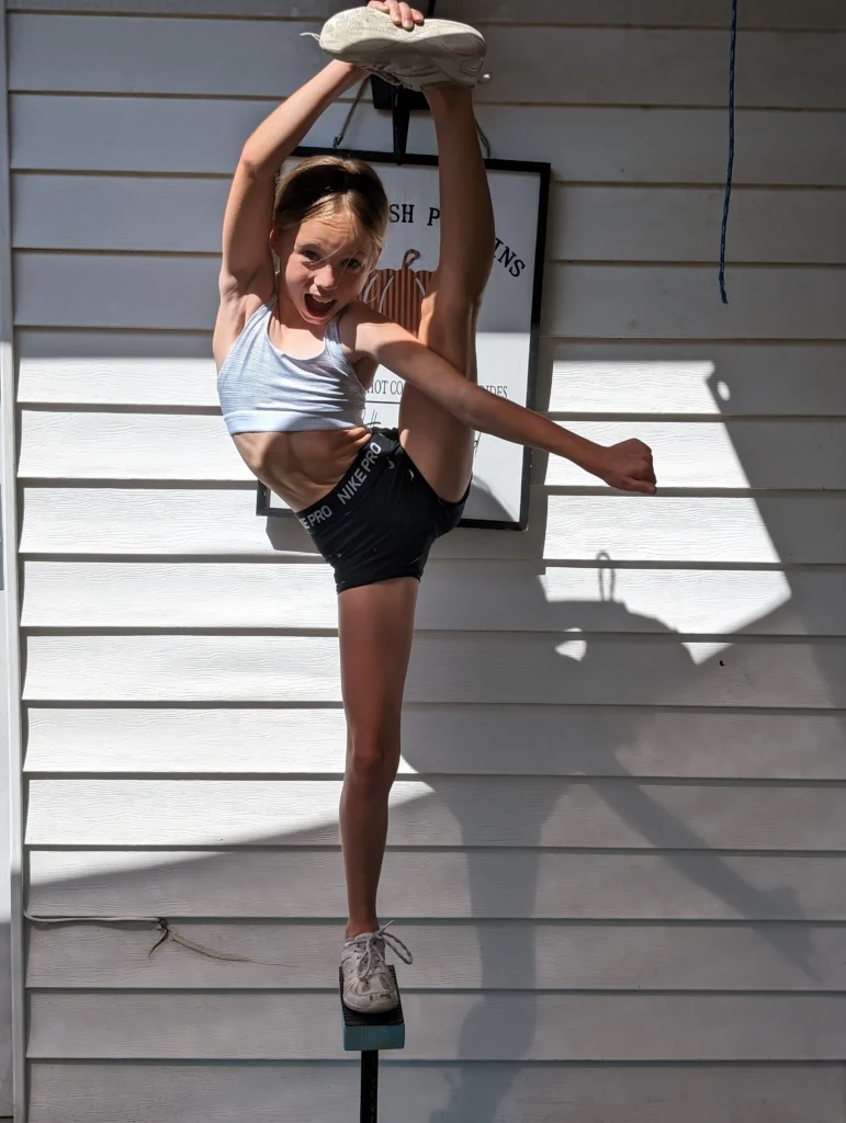 Kinsley holding a standing heel stretch against a white wall